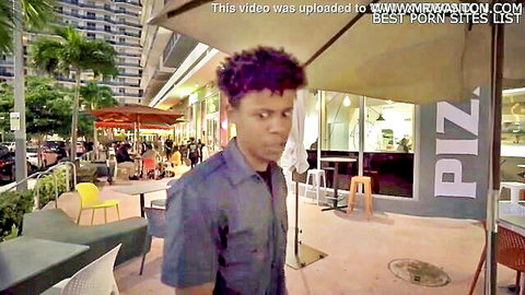 Ebony man with curly afro in purple shirt standing at outdoor pizza restaurant patio