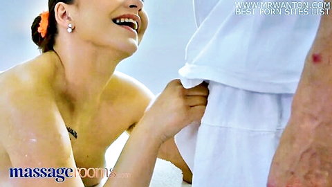 Smiling brunette masseuse pulls down man's white shorts in massage room