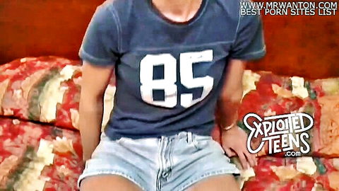 Teen with dreadlocks in gray t-shirt and denim shorts, sitting on couch - Exploited Teens preview