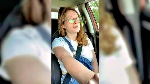 Busty redhead with glasses smiles showing deep cleavage in car overalls