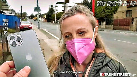 Mature woman with gray hair in pink mask holds phone on street, Extreme Streets vaginal prolapse