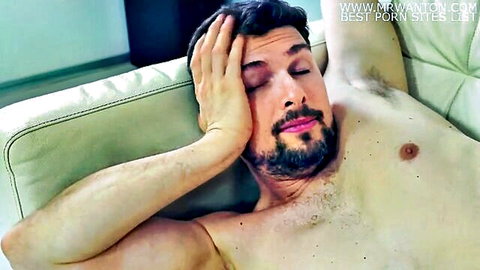 Muscular bearded hunk lying shirtless on couch with hand on forehead