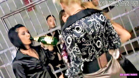 Brunette and blonde women in prison cell sharing champagne bottle, erotic scene