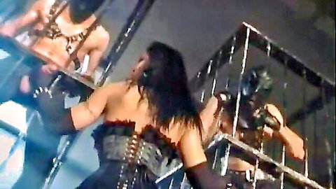 Brunette woman in black corset and gloves in BDSM scene with masked men