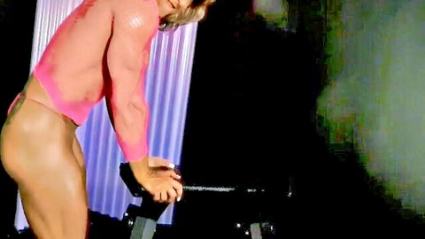 Muscular blonde in sheer pink lingerie bending over exercise bike