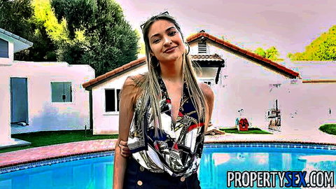 Blonde Latina babe with bangs smiling seductively in open scarf top teasing cleavage by pool