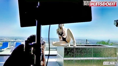 Blonde teen in skimpy black bikini spreads legs wide on rooftop pool balcony with city skyline during porn shoot