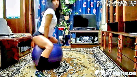 Sexy Asian woman teasing playfully on purple Pilates ball in shorts