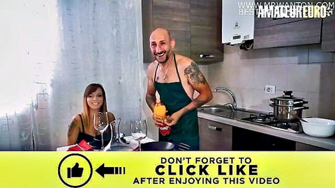 Bald tattooed hunk in green apron holds fruit smiling at sexy Asian woman in amateur kitchen