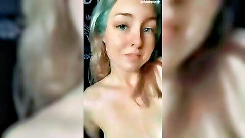 Teal-haired topless babe smirks seductively at camera showing bare shoulders and chest