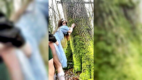 Amit in sheer blue dress hugging mossy tree outdoors, teasing pose with partner