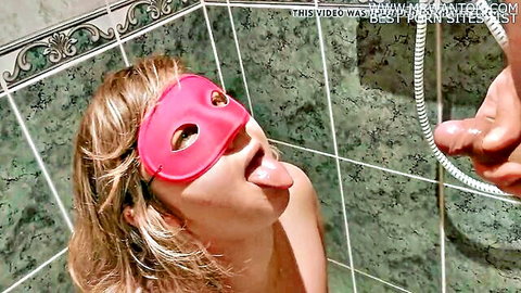 Blonde woman in pink blindfold kneels nude in shower with tongue out for oral action