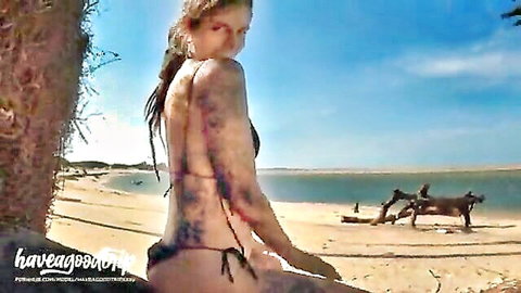 Topless Latina brunette with big tits sitting spread-legged on sunny beach in black thong