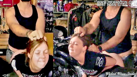 Muscular man in tank top roughly grabs redhead woman's hair forcing her face to his crotch in garage.