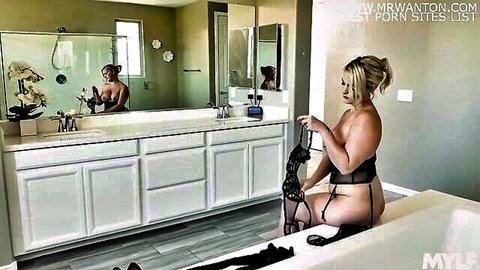 Busty blonde in black strappy lingerie teasing nude on tub edge