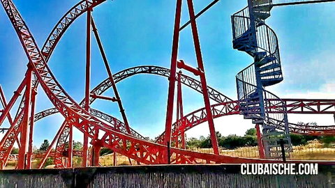 Towering red roller coaster tracks curving against blue sky with spiral staircase