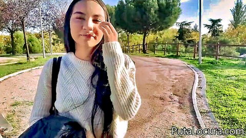 Cute Asian girl in white sweater smiling and touching face in sunny park