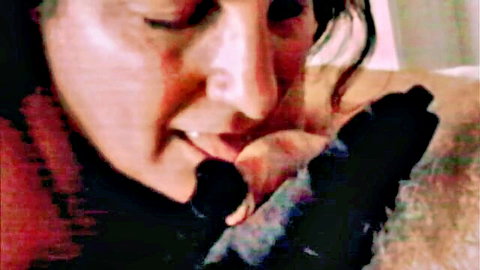 Brunette woman giving intense blowjob, gloved hands on shaft, close-up view