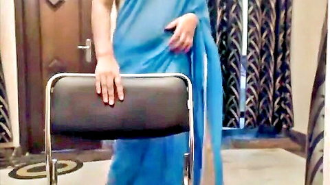 Sexy Indian woman in sheer blue sari teasing with hands on chair showing thighs