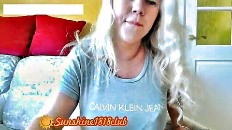 Blonde webcam girl smiling seductively in tight Calvin Klein shirt on bed