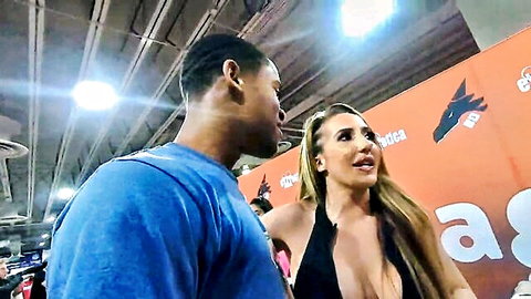 Busty blonde with huge tits in skimpy black dress flirts with handsome black man at Exxxotica event