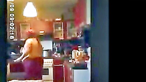 Cherie in orange top and purple skirt posing in kitchen from behind