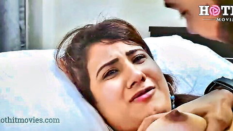 Indian girlfriend lying on bed looking upset as boyfriend grips her chest passionately