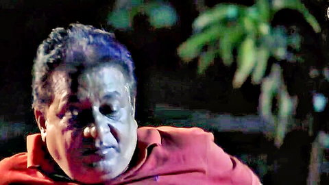 Close-up of mature South Asian man with intense expression wearing red hoodie outdoors at night