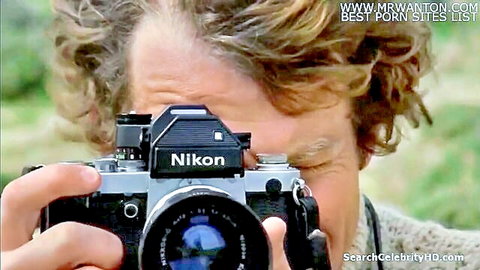 Blonde man peering through vintage Nikon camera lens outdoors