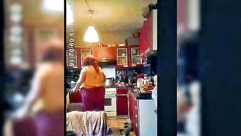 Redhead Cherie in orange top and red pants cooking from behind in kitchen
