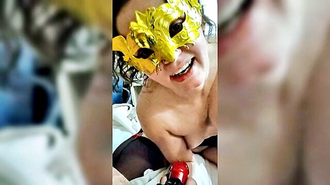 Topless masked woman in gold mask smiling, red glove for fisting locked slave