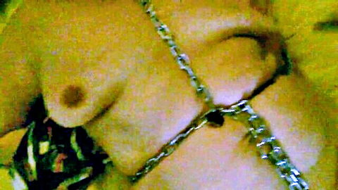 Submissive woman in tight chain head harness exposing pierced nipple in BDSM bondage