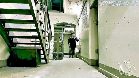 Dimly lit prison corridor with metal stairs and distant clothed mistress walking in femdom setting