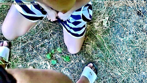 Blonde woman squats outdoors with striped shorts pulled aside fingering her shaved pussy POV