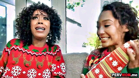 Two smiling ebony MILFs in tight red reindeer Christmas sweaters holding gifts on couch