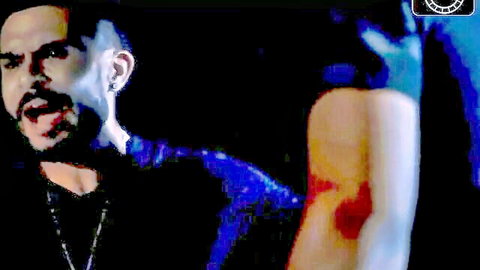 Intense close-up of muscular Latino man in black shirt with woman's gloved arm and stockinged leg