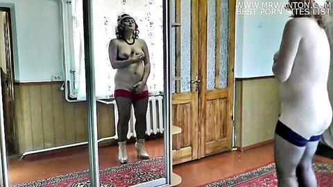Nude MILF with big tits stands in bedroom mirror exposing shaved pussy and ass in white stockings