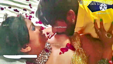 Passionate Desi newlyweds kissing intimately on honeymoon bed with rose petals
