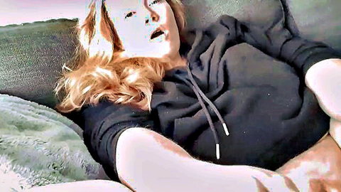 Blonde woman in hoodie lying back with open mouth, teasing oral expression