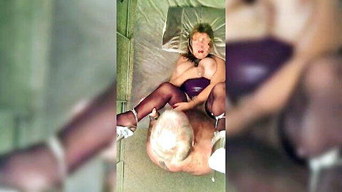 Mature MILF in purple PVC, stockings and high heels rides bald older man's cock with big natural tits exposed.