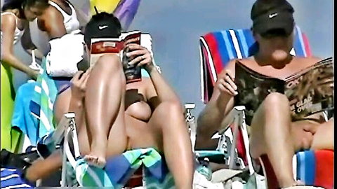 Topless couple on nude beach, strangers approach while reading books