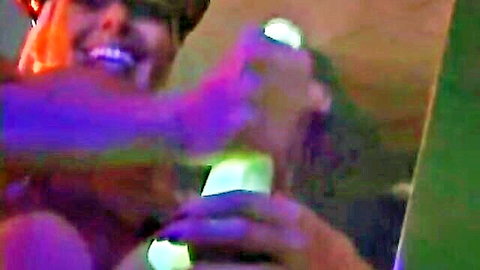 Smiling redhead femdom grips glowing green strapon dildo with both hands in neon glow