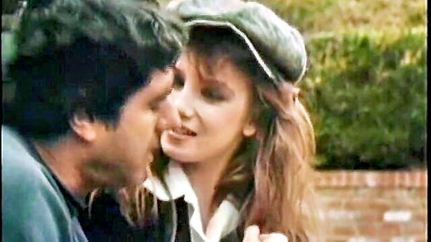 Blonde woman in green cap kissing dark-haired man in collared shirt