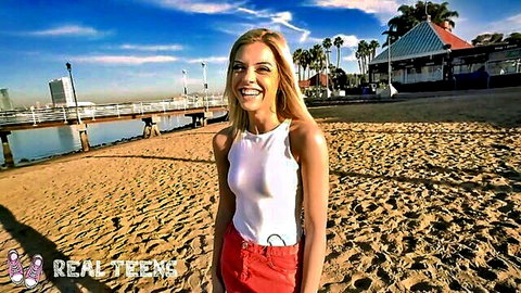 Allie Nicole blonde college teen smiling at sunny beach in white tank top and red shorts