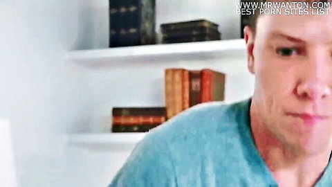Intense closeup of blonde stud in blue shirt against bookshelves in porn video