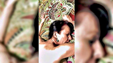 Mature brunette woman lying nude on bed in intense pose