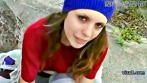 Cute brunette in blue beanie smiles teasingly wearing tight red top outdoors
