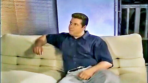Handsome man lounging seductively on couch in blue shirt and gray pants smirking