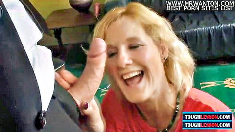 Blonde MILF laughs at thick pink cock head held by suited man in front of her smiling face