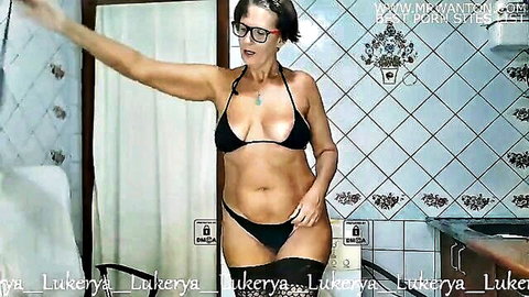 Mature brunette Lukerya in tiny black bikini top and thong posing sensually in bathroom with arms raised showing tits and curves